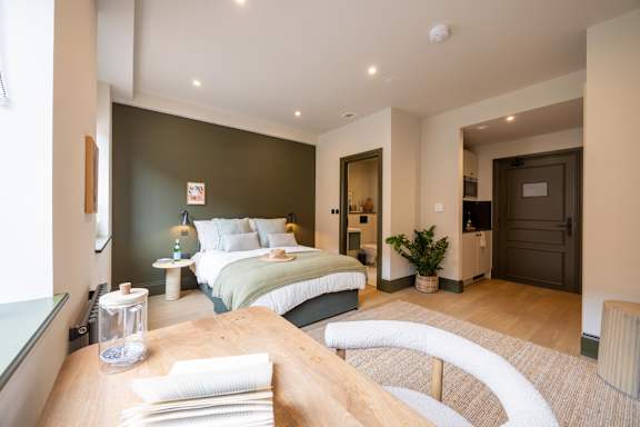 A bedroom with a bed, nightstand, and a table with a glass container on it.