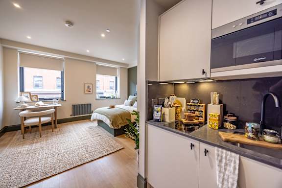 A kitchen with a microwave and a bedroom with a bed and a window.