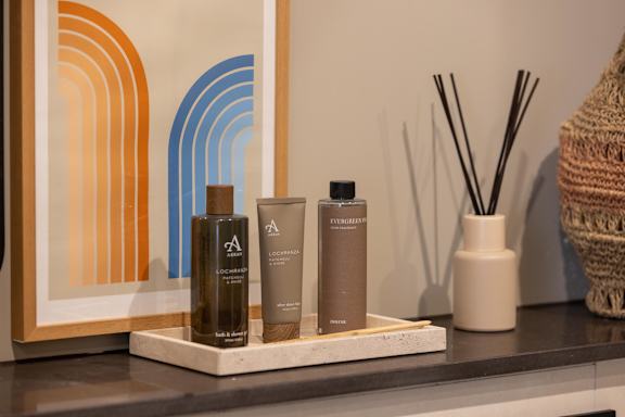 A bottle of Aesop Lock & Load body lotion sits on a shelf next to two other bottles.