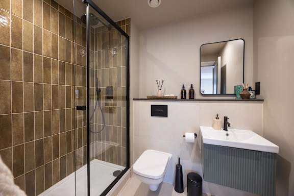 A bathroom with a brown tiled shower and a white toilet.