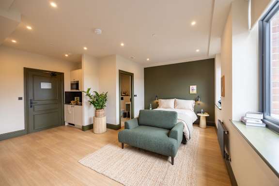 A room with a green couch and a bed with white bedding.