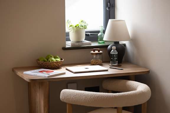 A desk with a laptop, a lamp, a plant, and a basket of fruit.