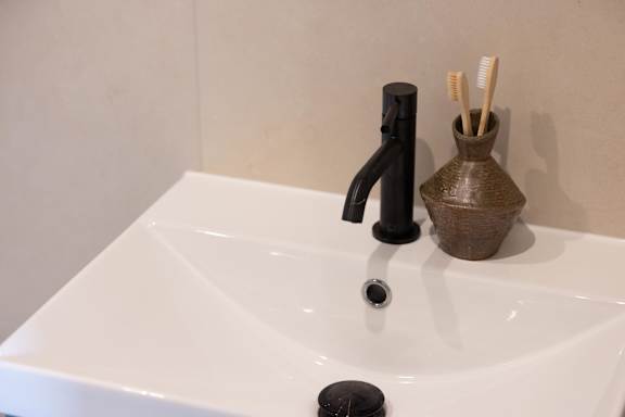 A white sink with a black faucet and a brown holder with toothbrushes in it.