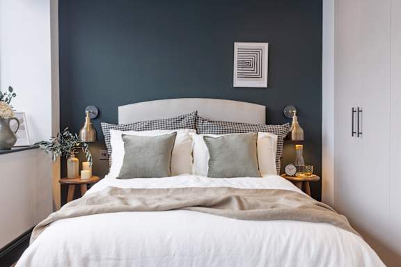 A bed with a white comforter and two grey pillows is in the center of the image.
