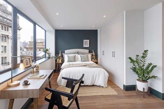 A bedroom with a bed, chair, and a table with a lamp on it.