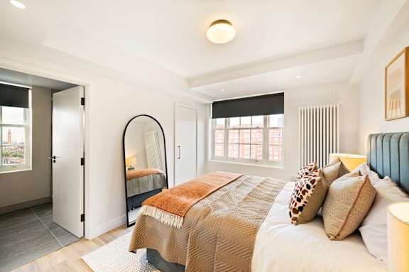 A bedroom with a bed, a mirror, and a window with blinds.