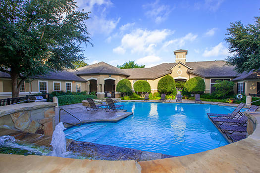 Resort-style pool with a stone water feature and lounge chairs in front of a tan clubhouse at Wade Crossing