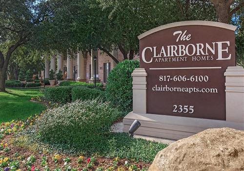 Stone monument sign for The Clairborne Apartment Homes with landscaping and trees behind it