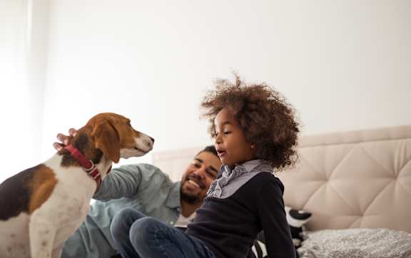A man and a child are sitting on a bed with a dog.