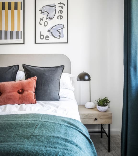 a bedroom with a bed with blue and orange pillows and a nightstand with