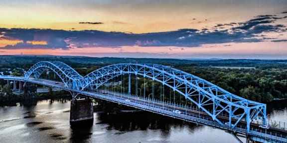 A blue bridge spans a river at sunset.