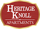 A sign that says "Heritage Knoll Apartments" in white text on a red background with a gold border.
