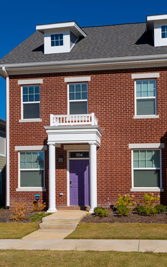 a brick house with purple doors and a sidewalk in front of it