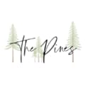 Black script writing The Pines with four pine trees in the background.