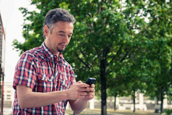 A man in a red and white checkered shirt is looking at his phone.