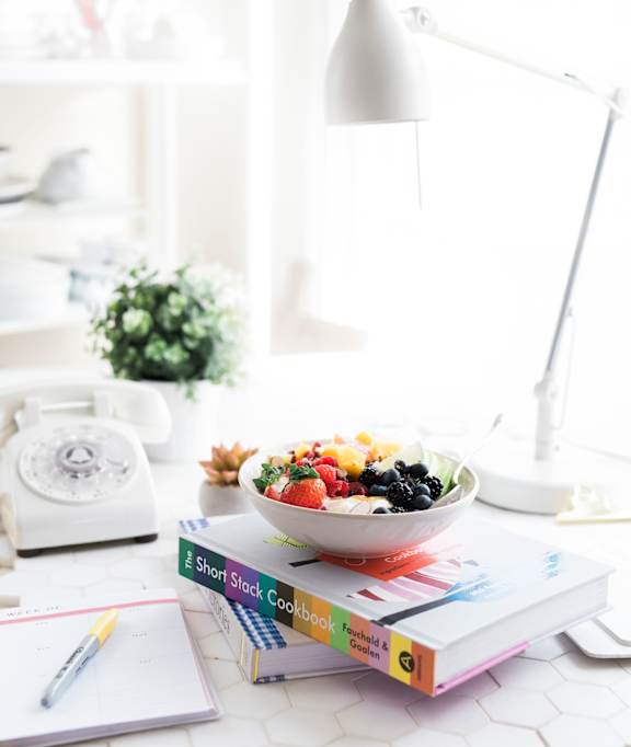 Bowl of fruit on stacked books beside a desk lamp in an apartment at Appletree Apartments.