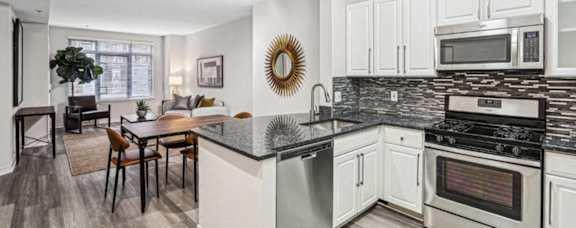 Modern open-concept apartment kitchen featuring white cabinets, granite countertops, stainless steel appliances, and adjacent dining area at The Barton at Woodley in Washington DC