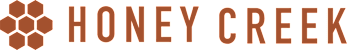 The image shows the text "HONEY CREEK" in brown letters with a hexagonal pattern in the background.