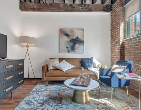 A living room with a blue couch, a grey cabinet, a TV, a painting, a floor lamp, a round table, and a rug.