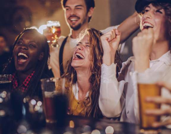 A group of people are laughing and enjoying drinks at a bar.