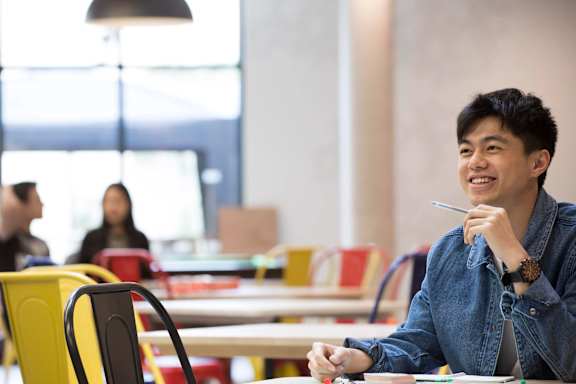 A man in a denim shirt is sitting at a table with a pen in his hand.