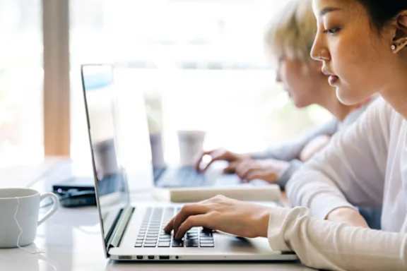 A woman is typing on a laptop in a brightly lit room.