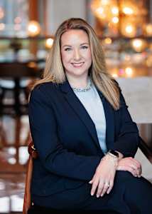 A woman in a black suit sits in a chair.