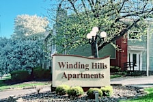 A sign for Windling Hills Apartments is in front of a house.
