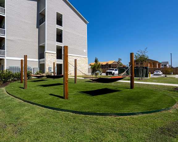 A beautiful outdoor area with green grass and hammocks in front of an apartment building