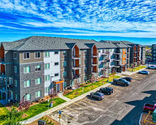 A row of modern apartment buildings with cars parked in the lot.