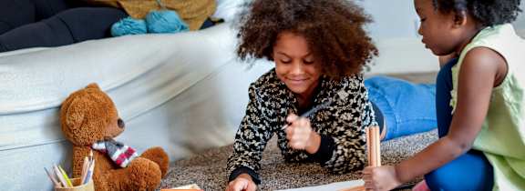 A woman and a child are drawing on the floor with colored pencils.