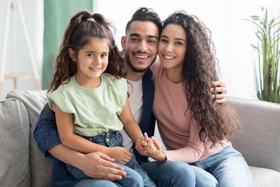 A family of three is sitting closely together on a couch.