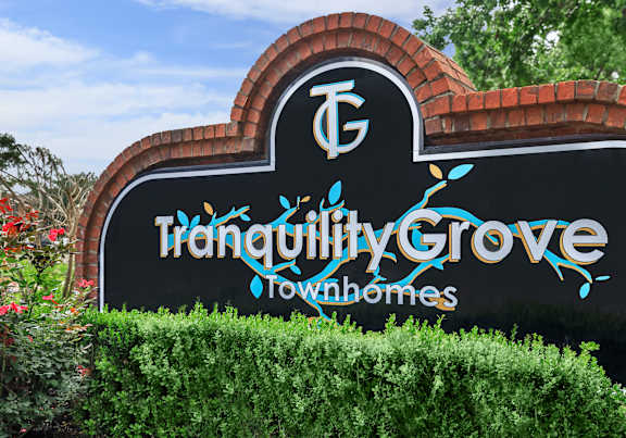 A sign for Tranquility Grove Townhomes is displayed in front of a hedge.