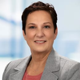 a woman with short hair wearing a gray suit and a pink shirt