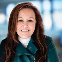 a smiling woman wearing a green jacket and a white turtleneck