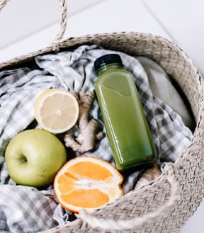 green apple, orange, and green drink in a basket with a blanket