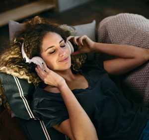 A woman with curly hair is wearing headphones and resting her head on a pillow.