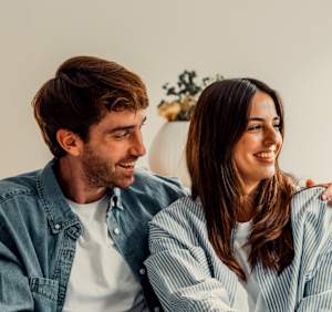 A man and a woman are sitting close together, both smiling and looking at each other.