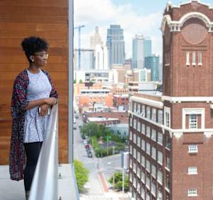 A woman stands on a balcony overlooking a cityscape.