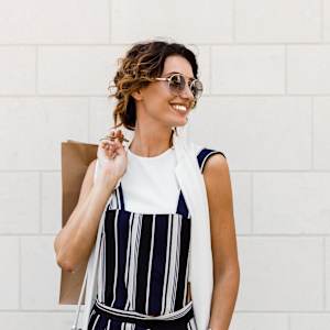 A woman in a striped dress is holding a brown paper bag.