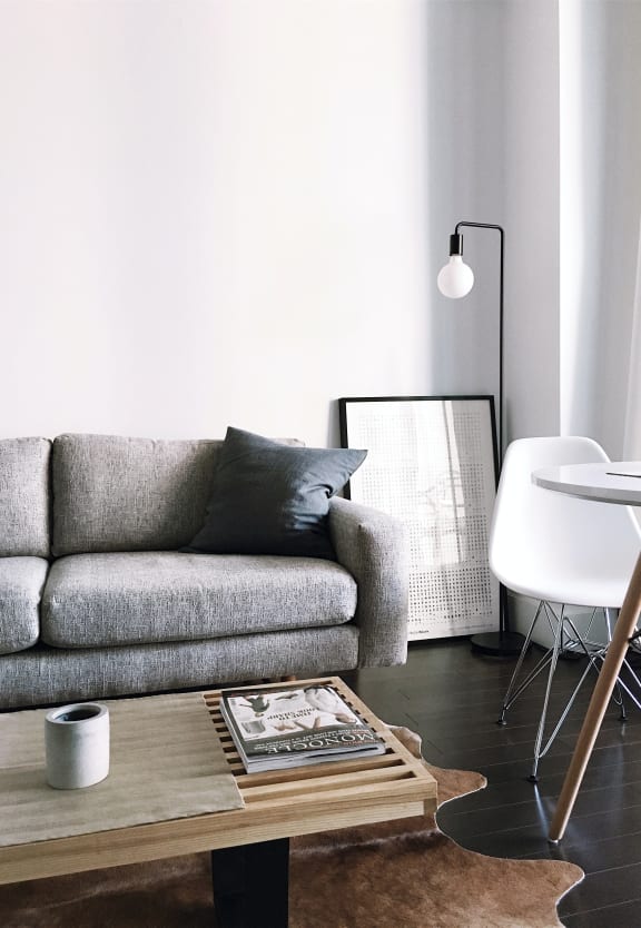Living room with grey couch, white walls, lamp in corner, light wood cofee table on dark wood floor.