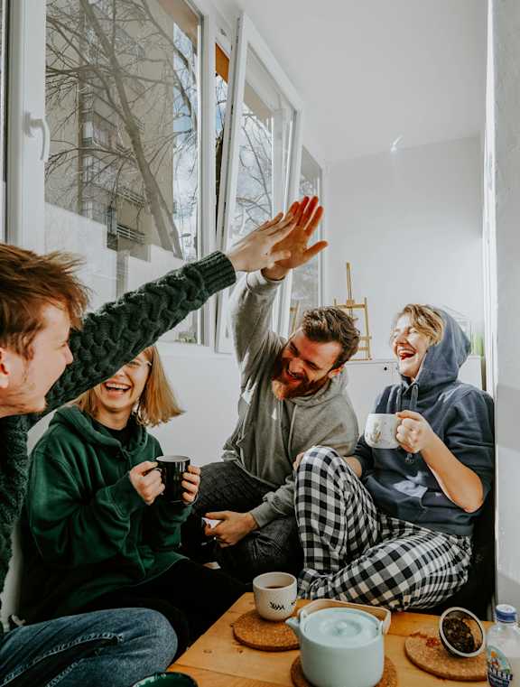 Four people in pajamas are sitting on the floor and high-fiving each other.