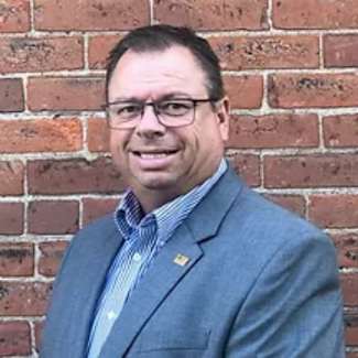 A man with glasses and a blue shirt is wearing a blue blazer.