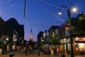 Photo of Church Street in Burlingtonat night. Church at background of image, small lit shops to left and right of church