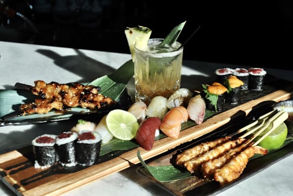 A variety of Japanese food including sushi, sashimi, and grilled items are displayed on a wooden board.