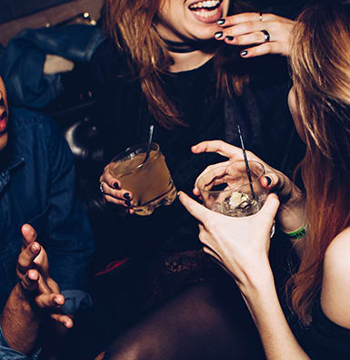 Three friends laughing over cocktails.