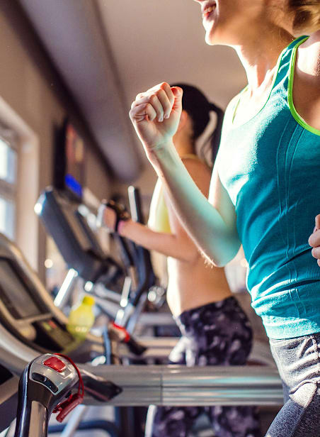 A woman in a blue tank top is running on a treadmill in a gym.