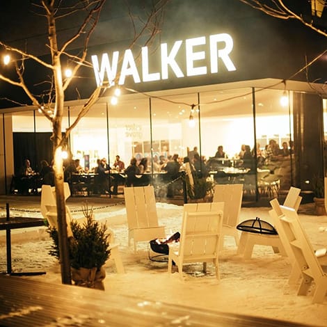 A outdoor patio to a busy restraurant that has a firepit surrounded by chairs.