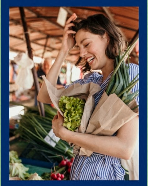 a woman laughing while holding a bowl of vegetables at a market at The Morgan Apartment Homes, Maryland