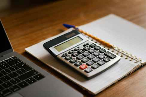 A calculator and a laptop are placed on a notebook with a pencil on top.